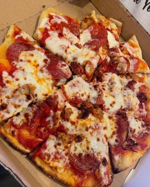 A pizza with pepperoni and melted cheese, sliced and placed in a cardboard box.
