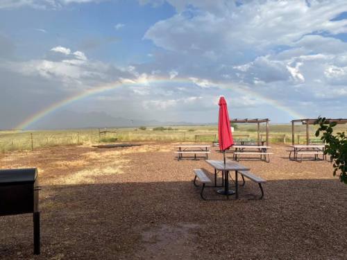 A picnic area with tables and a red umbrella, set against a backdrop of a rainbow and cloudy sky.