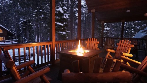 Cozy outdoor seating area with a fire pit, surrounded by snow-covered trees at dusk.