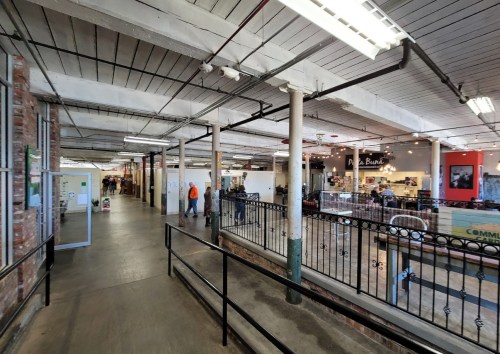 A spacious indoor market with exposed brick walls, vendors, and people walking along a wide corridor.