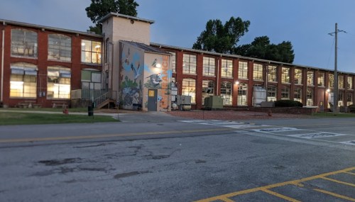 A brick building with large windows and a colorful mural, set against a twilight sky.
