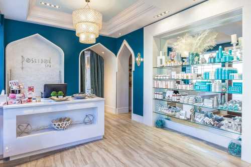 A modern spa reception area with a white desk, teal walls, and a display of skincare products on shelves.