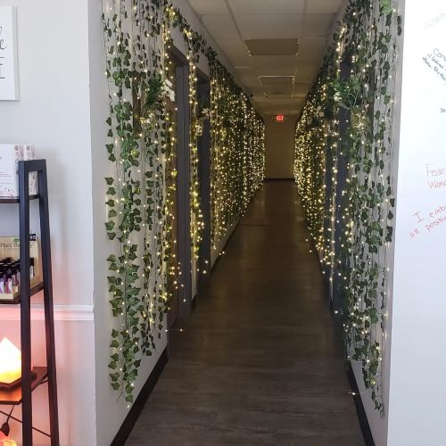 A well-lit hallway adorned with greenery and fairy lights, leading to a bright end.