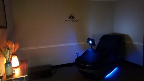 A dimly lit massage room featuring a massage chair, soft lighting, and a decorative table with a lamp.