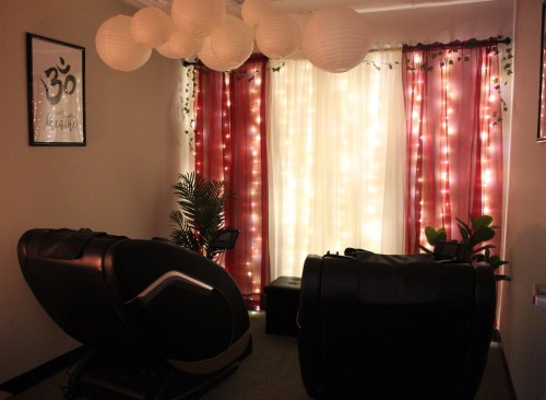 A cozy room with two massage chairs, soft lighting, and decorative curtains with fairy lights.
