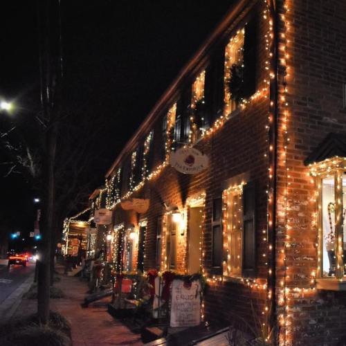 A charming street lined with brick buildings adorned with festive lights and decorations at night.
