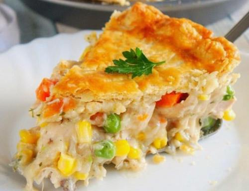 A slice of golden-brown chicken pot pie filled with vegetables and creamy sauce, garnished with a parsley leaf.
