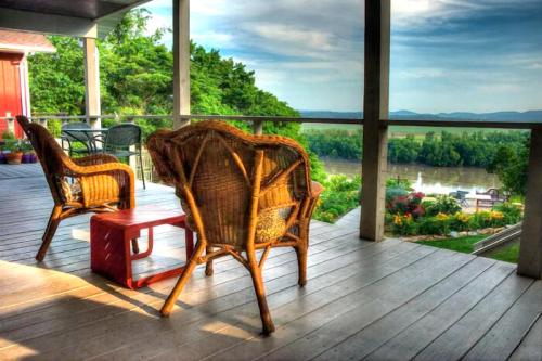 Two wicker chairs and a small table on a porch overlooking a scenic view of greenery and a river.