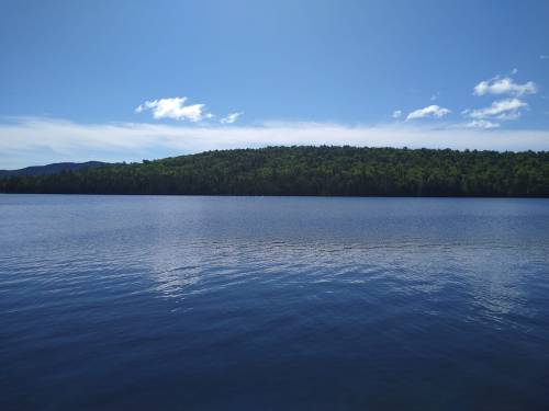 A serene lake reflecting a clear blue sky and lush green hills in the background.