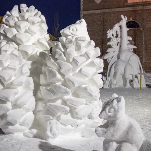Snow sculptures of pine trees and a bear, with a whimsical design, set against a nighttime backdrop.