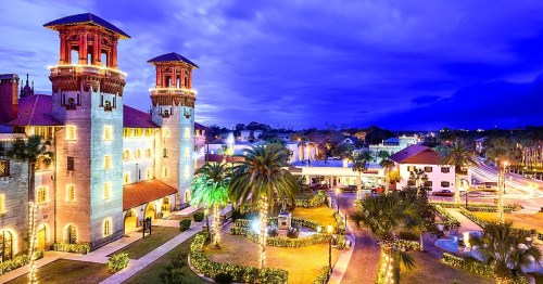 A beautifully lit historic building at dusk, surrounded by palm trees and festive decorations.