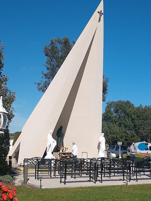 A modern monument with a tall, triangular structure, surrounded by statues and benches in a serene outdoor setting.