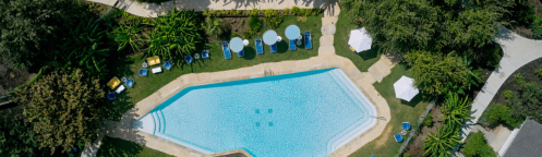 Aerial view of a swimming pool surrounded by greenery, lounge chairs, and umbrellas in a serene outdoor setting.