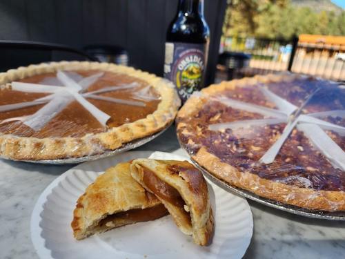 Two pies on a table, one pumpkin and one pecan, with a slice of pie and a bottle of soda in the background.
