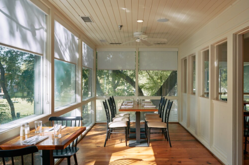 Bright, airy dining area with wooden tables and chairs, large windows, and natural light filtering through.