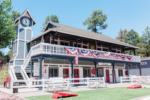 A two-story building with a clock tower, decorated with red, white, and blue bunting, surrounded by trees.
