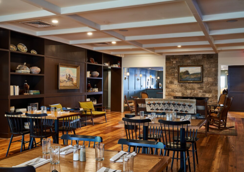 Cozy restaurant interior with wooden tables, black chairs, a stone fireplace, and decorative shelves.
