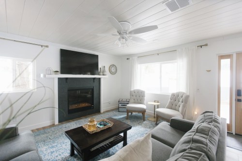 Cozy living room with a fireplace, two armchairs, a coffee table, and a large TV on the wall, featuring light decor.