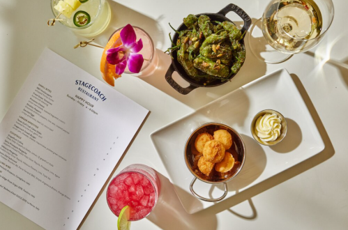 A table setting with cocktails, a dish of shishito peppers, shrimp, and a dessert, alongside a restaurant menu.