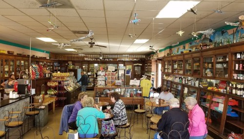 A cozy café interior with wooden shelves, model airplanes hanging from the ceiling, and patrons enjoying their meals.