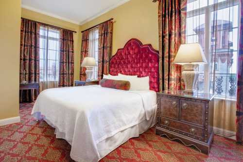 Cozy hotel room featuring a queen bed, decorative curtains, bedside tables, and large windows with natural light.