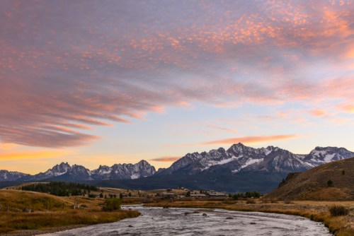 Scenic view of mountains at sunset, with colorful clouds reflecting in the sky above a calm river.