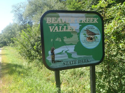 Sign for Beaver Creek Valley State Park featuring a fishing scene and a depiction of a Louisiana waterthrush.