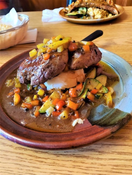 A plate of grilled meat topped with colorful salsa, served over mashed potatoes and accompanied by sautéed vegetables.