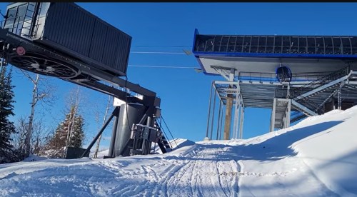 Ski lift station with a loading area and snowy landscape under a clear blue sky.