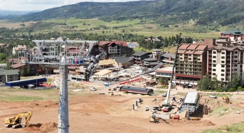A construction site with heavy machinery, buildings, and a ski lift in a mountainous landscape.