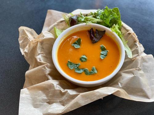 A bowl of orange soup garnished with leafy greens arranged to form a smiling face, served on crumpled paper.