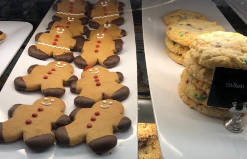 A display of gingerbread cookies with chocolate bottoms and red buttons, alongside a stack of colorful cookies.