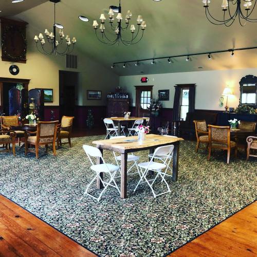 A cozy room with wooden floors, floral carpet, tables, chairs, and chandeliers, creating a warm, inviting atmosphere.