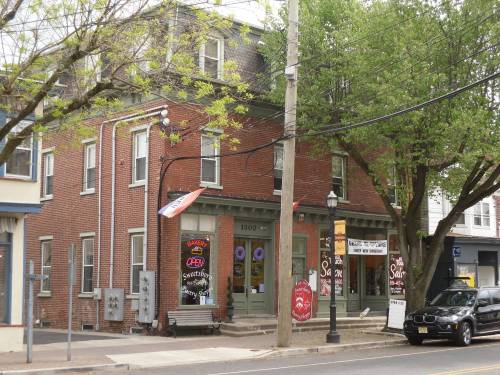 A brick building with large windows, signs, and trees nearby, located on a street with power lines and a lamp post.