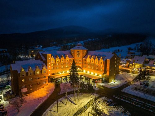 A warmly lit hotel surrounded by snow, set against a dark, mountainous backdrop at night.