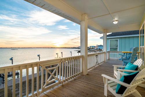 A serene waterfront view from a porch at sunset, featuring wooden chairs and a peaceful atmosphere.