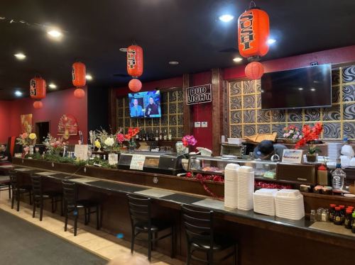 A cozy restaurant interior with a bar, red lanterns, and a TV, featuring floral decorations and a warm atmosphere.