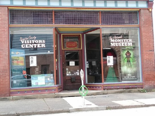 Exterior of a brick building featuring signs for a Visitors Center and a Monster Museum, with a parking meter in front.