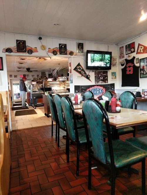 A cozy diner interior with green chairs, a TV, and vintage decor, featuring a counter and a customer in the background.
