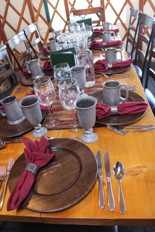 A beautifully set dining table with wooden plates, silverware, and burgundy napkins in a cozy yurt setting.