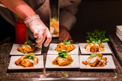 A chef garnishes plates of enchiladas with sauce and fresh herbs in a restaurant setting.
