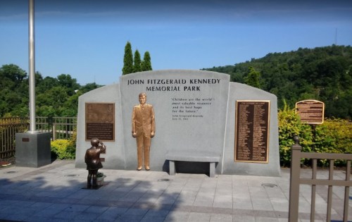 A memorial park featuring a statue of John F. Kennedy and a quote about children, surrounded by greenery.