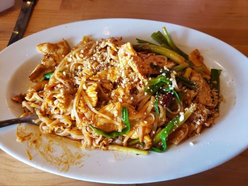 A plate of stir-fried noodles with chicken, green onions, and sesame seeds.