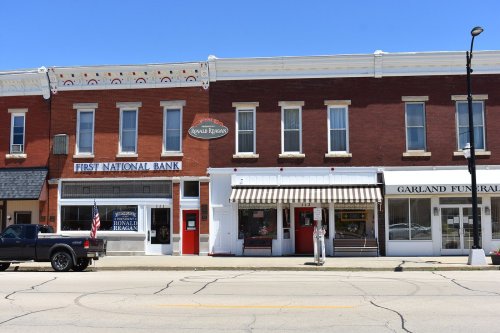 A street view of a small town featuring a bank, a funeral home, and a restaurant, with clear blue skies above.