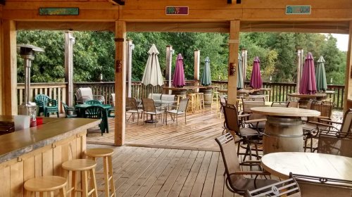 Outdoor seating area with wooden deck, tables, chairs, and umbrellas in a relaxed, inviting atmosphere.