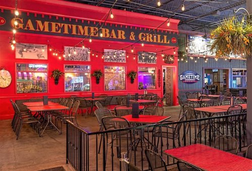 A vibrant bar and grill with red walls, outdoor seating, and string lights, creating a lively atmosphere.