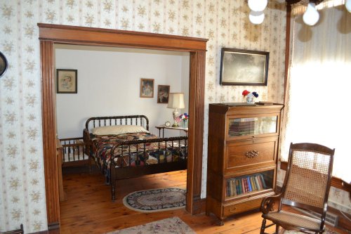A vintage bedroom with a metal bed, wooden furniture, floral wallpaper, and a cozy reading nook.
