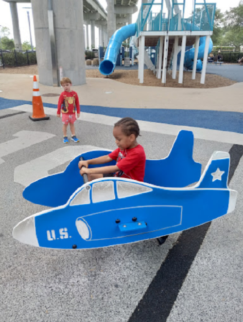 A child plays in a blue airplane structure at a playground, while another child watches nearby.