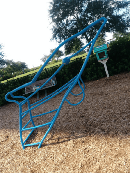 A blue playground climbing structure shaped like a rocket, surrounded by wood chips and greenery.