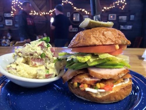 A close-up of a sandwich with lettuce, tomato, and turkey, served with a side of potato salad on a blue plate.